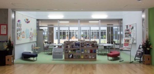 大きな窓ガラスのある部屋の中央にマガジンラックや新聞ラック、ソファが設置された1階メディアセンターの写真