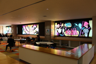大きなステンドグラスの作品が飾られた室内で、複数の学生などが椅子に座っている写真