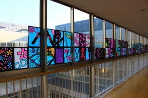 廊下の窓に卒業証書やカラフルな花などが描かれたステンドグラスの作品が飾られている写真