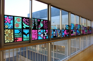 廊下の窓に、ボールや桜の木々など描かれたステンドグラスの作品が飾れている写真