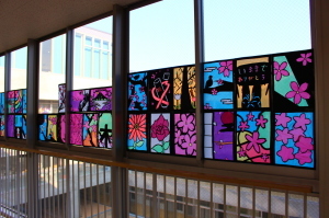 廊下の窓に、植物や木々が描かれたステンドグラスの作品が飾れている写真