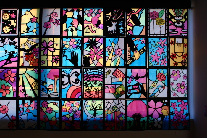 花や蝶、鳥や動物、バスケットゴールなどが描かれた36枚のステンドグラスの作品の写真