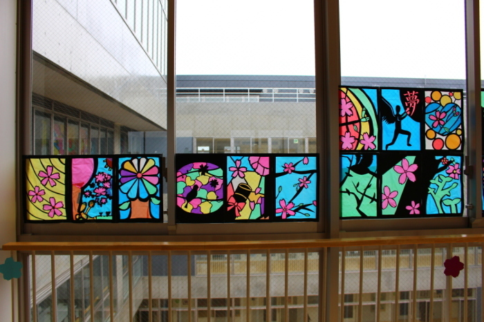 廊下の窓に、カラフルな木や桜の花火あらなどが描かれたステンドグラスの作品が飾られている写真
