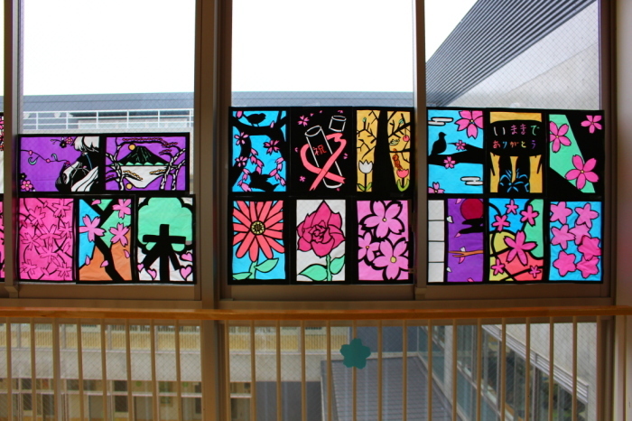桜の木や花びら、花が描かれたステンドグラスの作品が窓に飾られている写真