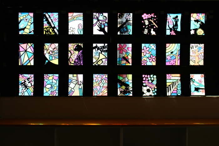 幾何学模様や、蝶、鍵盤や楽器などが描かれた24枚のステンドグラスの作品の写真