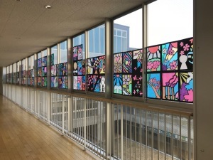 長い廊下の右側の窓に、カラフルなステンドグラスの作品が飾られている写真