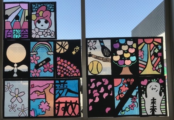 マイメロディや、月と鶴、桜やラケットとテニスボールなどが描かれたステンドグラスの作品が窓に飾られている写真