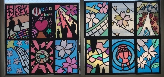 花びらと鳥、音符や、歩いている人の後ろ姿などが描かれたステンドグラスの作品の写真