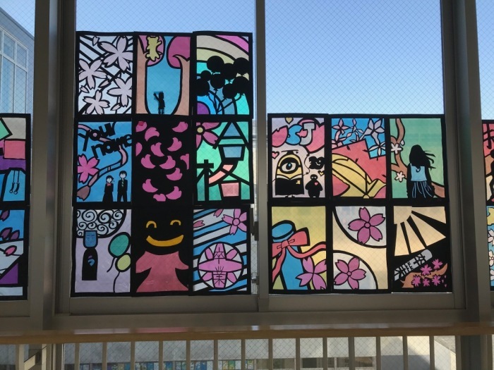 ミニオン、卒業証書、桜の花びら、風船などが描かれたステンドグラスの作品が窓に飾られている写真