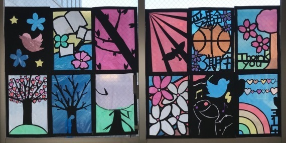 虹、ハートの花びらの木、本やボールなどが描かれたステンドグラスの作品の写真