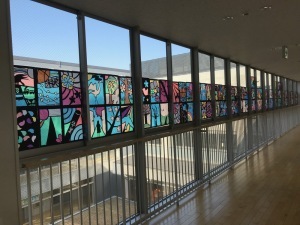 長い廊下の左側の窓に、カラフルなステンドグラスの作品が飾られている写真