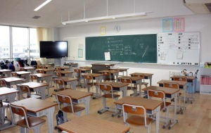 黒板の左側に大画面のテレビが設置され机と椅子が並んでいる教室内の写真