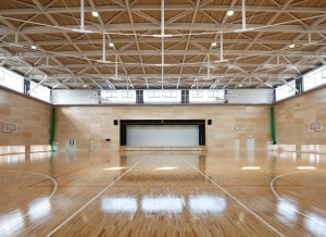 中央奥にステージがあり壁上の大きな窓から光が差し込み明るい室内の体育館の写真