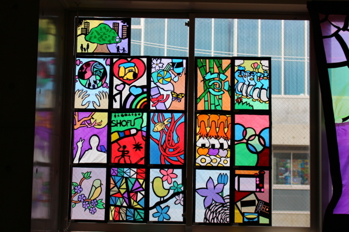 魚や、おにぎり、ペンギンなどが描かれたステンドグラスの作品が窓に飾られている写真