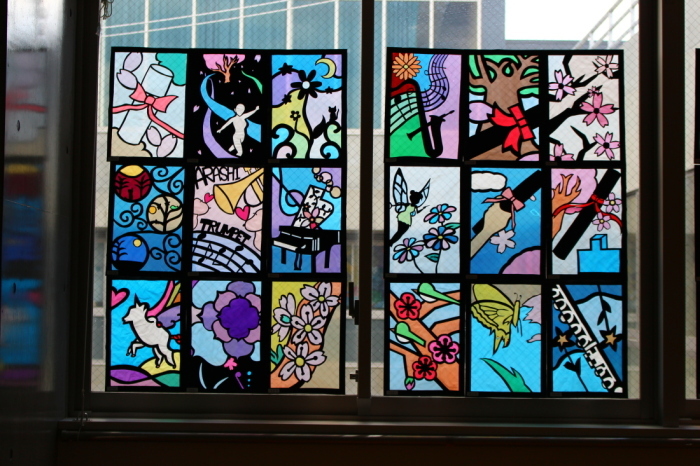 ピアノや、卒業証書、桜などが描かれたステンドグラスの作品が窓に飾られている写真