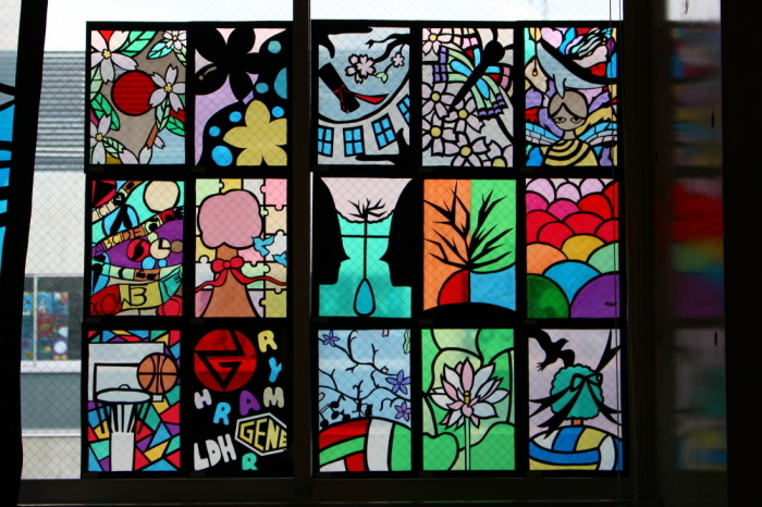 バスケットや、花、いくつもの半円が描かれたステンドグラスの作品などが窓に飾られている写真