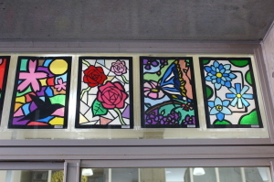 赤やピンク、水色の花や鳥が描かれた4枚のステンドグラスの作品の写真