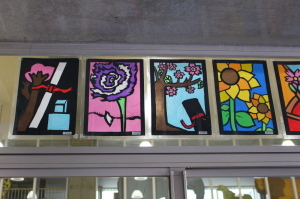 桜の木、紫の花、桜の木の下の黒い筒、ひまわりが描かれた4枚のステンドグラスの作品の写真