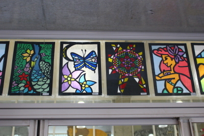 森の中のクジャク、蝶やマーメイド、万華鏡の中身のような柄が描かれた4枚のステンドグラスの作品の写真