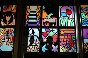 花や、女の子鳥などが描かれたステンドグラスの作品が並んでいる写真