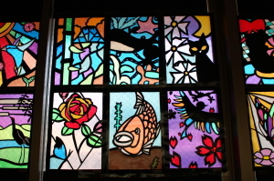 薔薇の花や、鯉、黒い猫などが描かれたステンドグラスの作品が並んでいる写真