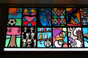 桜の木、木にとまった鳥、キリン、鳥やサッカーボールなどが描かれているステンドグラスの作品が並んでいる写真