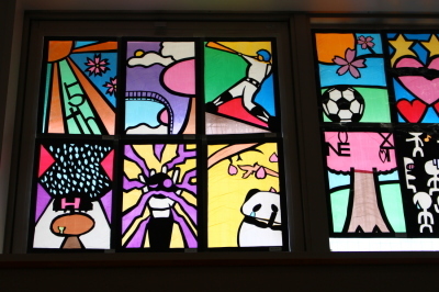 涙を流すパンダ、バットを振る少年、サッカーボールなどが描かれているステンドグラスの作品が並んでいる写真