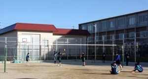 左奥にバスケットゴールがあり手前に設置されたバレーのネットの周りで生徒たちがストレッチやバレーの練習を行っている北グラウンドの写真