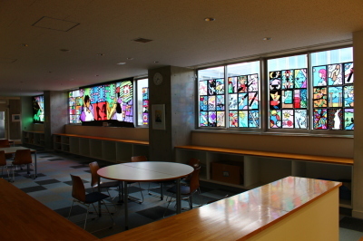 室内の窓いっぱいに飾られた大きなステンドグラスの作品や女の子や風景などが描かれた作品の写真