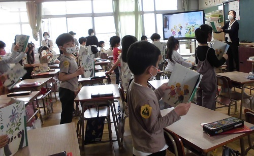 児童たちが自席に立って国語の教科書を読んでいる授業参観の様子の写真