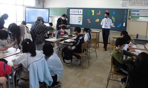 グループごとに分かれて座っている児童と保護者が一緒に「ペントミノ」を行っている授業参観の様子の写真