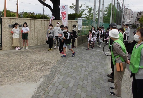 校門の外に立っている児童と民生児童委員の方々の間を元気に挨拶して登校してくる子供たちの写真