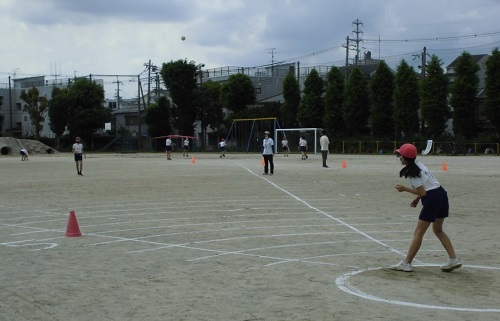 運動場に消石灰で円を書いた場所から女子児童がボールを投げている写真