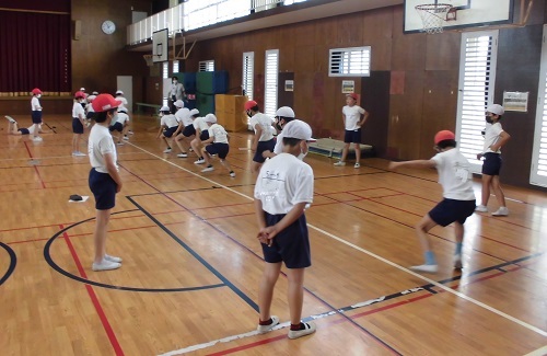 体育館内で児童が一列に並んで反復横跳びを行っている様子の写真