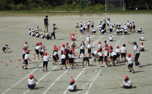 赤色と白色の帽子に分かれた児童たちが玉入れを行っている写真