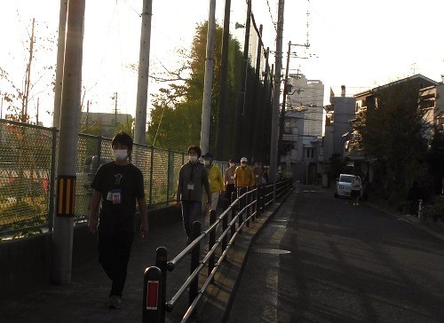 学校の外側の歩道を防犯パトロールを行う方々が間隔をあけて1列で歩いている写真