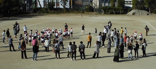 校庭に体操着を着た児童と保護者が立っている体育の授業参観の様子の写真
