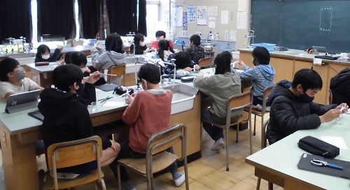 教室の席に座っている児童たちが理科の実験を行っている様子の写真