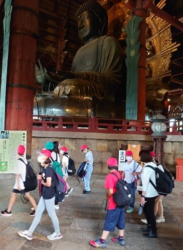 東大寺の本尊である盧舎那仏坐像の近くを歩いて見学している先生と児童たちの写真
