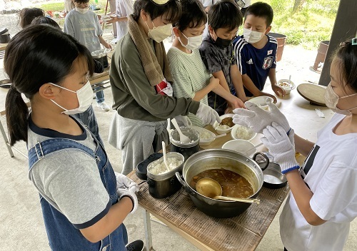 飯ごうで炊いたご飯と鍋で作ったカレーを容器に移している児童たちの写真