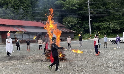 大きな炎の周りを4名の児童が松明を持って歩いているキャンプファイヤーの様子の写真