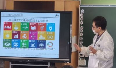 SDGs17の目標のマークがディスプレイに写しだされ、男性教師が授業を行っている写真
