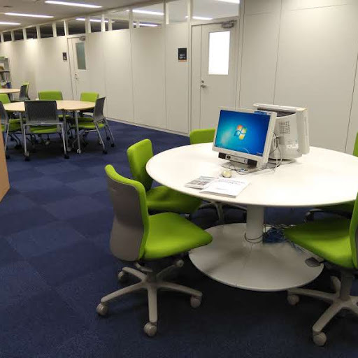 白い丸テーブルと椅子が複数組あり、その一つには利用者がDVDを閲覧するためのパソコンが設置されているライブラリー閲覧スペースの一角の写真