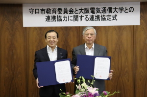 右に首藤教育長、左に大石理事長・学長が協定書を持って立っている様子を写した写真
