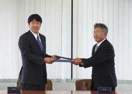 左に奥田学長、右に藤川教育長が協定書を交換している様子を写した写真