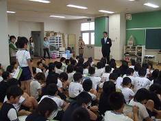 大勢の守口小学校の児童が講師の前で体育座りをし、そのなかの一人の児童が立って講師に質問している様子を写した写真