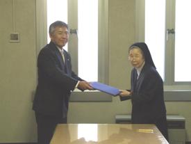 左に藤川教育長、右に縄田学長が協定書を交換する様子を写した写真