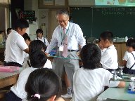 大阪工業大学の先生が、不思議な物体をゆっくり引っ張って伸ばしているところを守口小学校の児童が見ている様子を写した写真