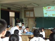 大阪工業大学の先生が、不思議な物体で机を叩いているところを守口小学校の児童が見ている様子を写した写真