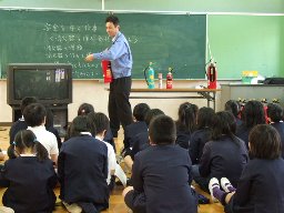 橋波小学校の児童が、実物を使った初田製作所の講師の説明を体育座りで聞いている様子を写した写真